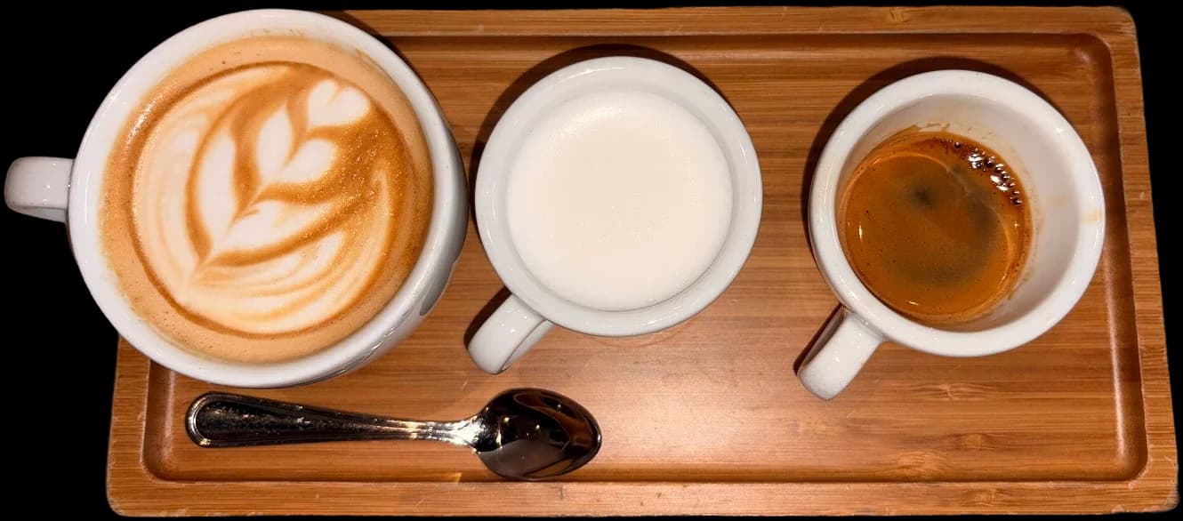 A wooden tray with a latte, a small cup of steamed milk, and an espresso